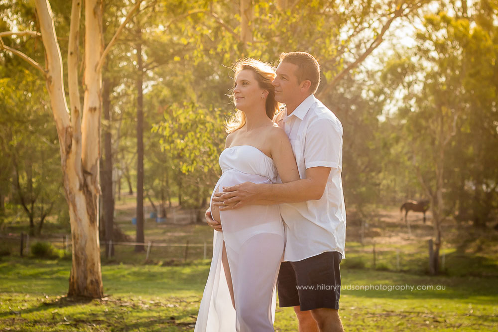 A pregnant wife and her adoring husband, gazing into the distance in the afternoon sun